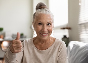 Woman with implant dentures in South Windsor giving thumbs up 