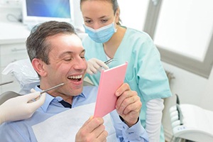 man at dentist’s office admiring his smile in a mirror