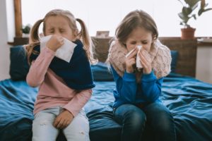 two children blowing their noses during cold and flu season 