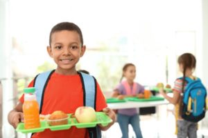 Child smiling and holding his school lunch.