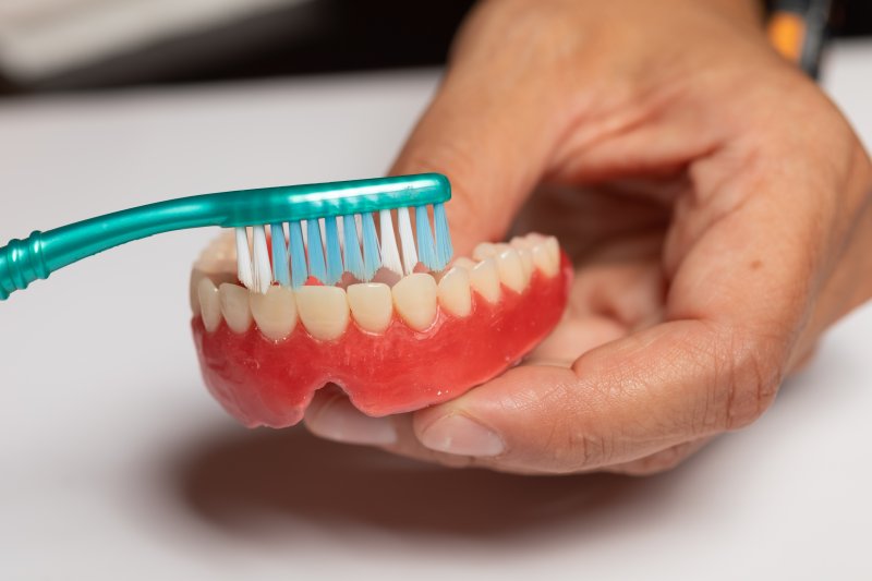 patient cleaning dentures with a toothbrush