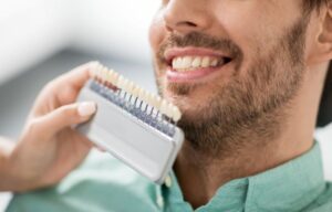 Dentist holding shade guide next to patient’s teeth 
